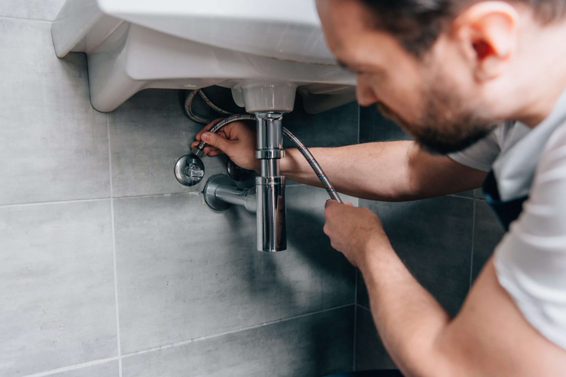 selective focus of male plumber in working overall fixing sink in bathroom new